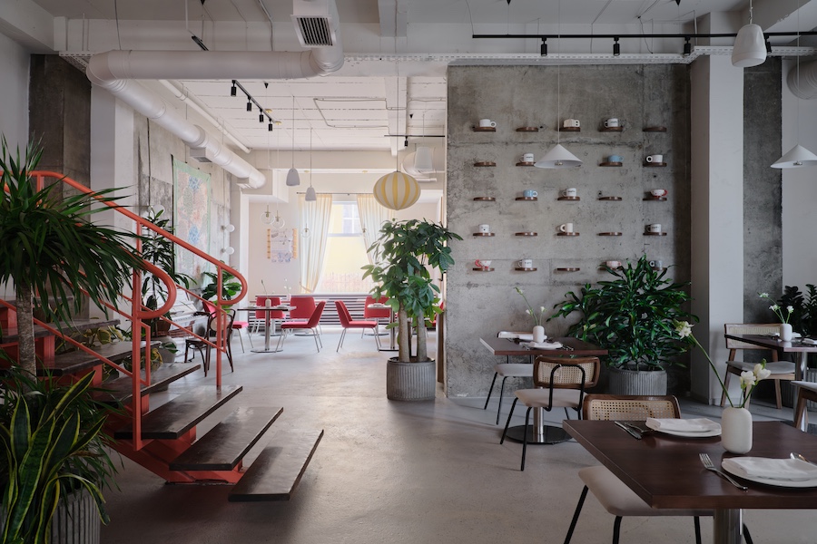 Capito Café Bishkek Kyrgyzstan industrial loft raw concrete walls exposed pipes wall art pink chairs yellow white lantern lights staircase indoor plants